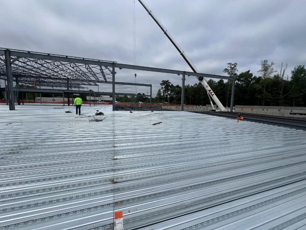 Corrugated steel roof decking installation with crane in background